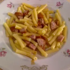 Eine schnelle Nudelpfanne mit Wurststücken auf einem Teller mit Blumenmuster.