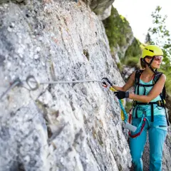 Kobieta w kasku i sprzęcie wspinaczkowym pokonuje via ferrata niemcy. Wspinaczka po skalnej ścianie z asekuracją.