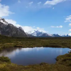 Spokojne jezioro odbija ośnieżone góry, w tym majestatyczne góry z Aconcagua, otoczone zielonymi wzgórzami pod błękitnym niebem.