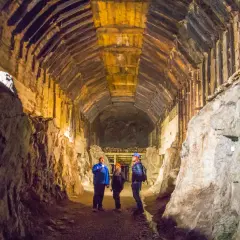 Trzech turystów z latarkami eksploruje mroczny, drewniany tunel. To część podziemnego riese kompleksu, gdzie historia miesza się z tajemnicą.