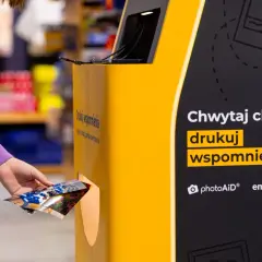 Ręka wkłada zdjęcia do automatu, by wydrukować wspomnienia w Empiku.