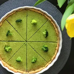 Zielona tarta z brokułami, pokrojona na 8 kawałków, ozdobiona różyczkami brokułów. Obok żółty tulipan.