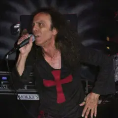 Ronnie James Dio zespół śpiewa do mikrofonu, ubrany w czarną koszulkę z czerwonym krzyżem.