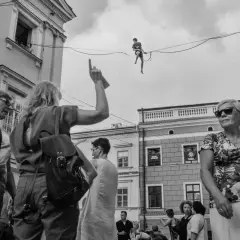 Uliczna fotografia: człowiek balansuje na linie, tłum obserwuje z dołu.