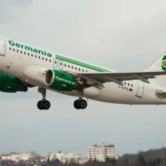 Samolot linii lotniczych Germania z zielonym logo startuje na tle pochmurnego nieba.