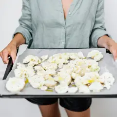 Kobieta trzyma blachę z pokrojonym kalafiorem, przygotowanym do pieczenia. To zdrowy posiłek, idealny na dietę.