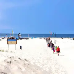 Menschen spazieren auf einem Holzsteg über den weiten, weißen nordsee strand. Der Himmel ist blau, das Meer ruhig.