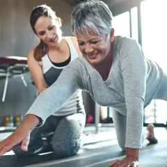 Une femme âgée sourit en faisant un exercice de renforcement avec l'aide d'une coach. Le sport est essentiel pour la rééducation après un cancer du sein.