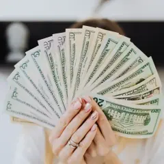 Dłonie trzymają wachlarz banknotów dolarowych. Szukasz firm, kto udziela finansowania firmom bez BIK?
