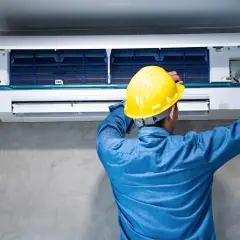 Técnico con casco amarillo trabajando en un aire acondicionado para quitar pitido.