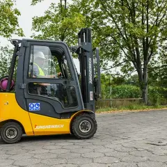 Żółty wózek widłowy Jungheinrich z kierowcą w kamizelce odblaskowej i kasku na zewnątrz.