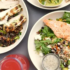 Två skålar med proteinrik mat: grillad kyckling med vildris och grönsaker, samt lax med sallad, nötter och ost. En röd dryck syns också.