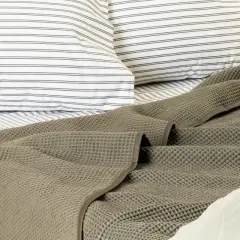 A textured, grey blanket is draped at the end of a bed, over striped pillows and sheets.