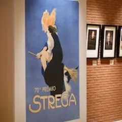 Un poster vintage celebra il 70° Premio Strega, con ritratti di autori appesi su una parete di mattoni.