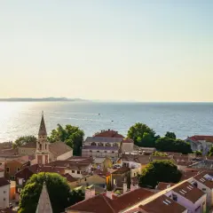 Widok na dachy Zadar i okolice, z kościelną wieżą górującą nad miastem i błękitnym morzem w tle.