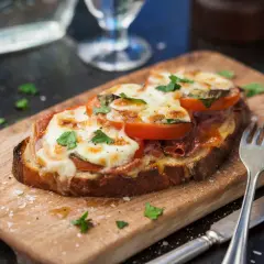 En härlig tallrik med varma mackor, toppad med smält ost, tomater och färska örter. Serveras på en träskärbräda med bestick.