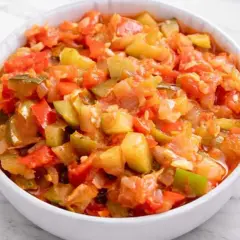 Un tazón blanco lleno de pisto manchego, un guiso vibrante de verduras picadas como tomate, pimiento y calabacín.