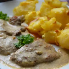 Pyszny karczek w sosie chrzanowym z pieczonymi ziemniakami. Danie ozdobione natką pietruszki.