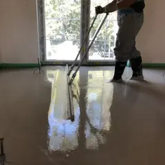 Pracownik wylewa beton, wyrównując go łaty. To kluczowe dla obliczenia, ile potrzeba cementu na 1m2 wylewki.