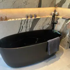 Baignoire noire en acrylique, prête pour un nettoyage. Un drap de bain gris est accroché.