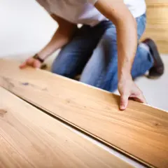 Uomo in ginocchio posa assi di legno per un pavimento con schema a spina di pesce.
