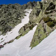 Canal de nieve y roca en la ladera de la Maliciosa, con vegetación escasa y un cielo azul intenso.