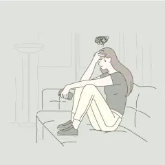 Ragazza seduta sul divano, con la mano sulla fronte e un groviglio di pensieri sopra la testa. Si sente persa, proprio come quando sto a casa sto male.