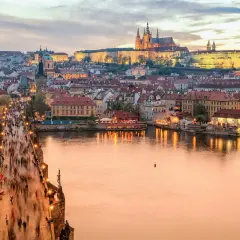 En folktät Karlsbro i Prag vid skymningen, med upplysta byggnader och Pragborgen i bakgrunden. En klassisk vy att se i Prag.