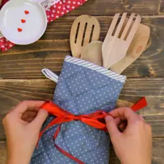 Idee regalo fai da te: un set di utensili da cucina in legno, avvolto in un guanto da forno a pois e legato con un nastro rosso.