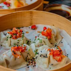 Délicieux dim sum à Paris, servis dans un panier en bambou, garnis de garnitures vibrantes et de graines de sésame.