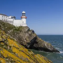 Biała latarnia morska na skalistym klifie nad morzem, Irlandia.