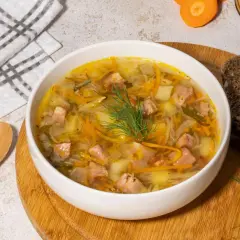 Aromaticzny kapuśniak ze słodkiej kapusty z kawałkami mięsa, ziemniakami i marchewką, udekorowany koperkiem. Obok kromki ciemnego chleba.