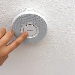 Finger drückt auf den X-Sense Rauchmelder, um den Test zu starten. Sicherheit geht vor!