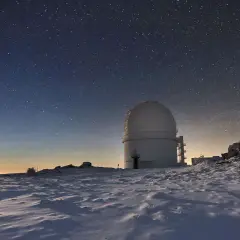 Observatorio en el calar alto bajo un cielo estrellado. La luna ilumina un paisaje nevado y rocoso.