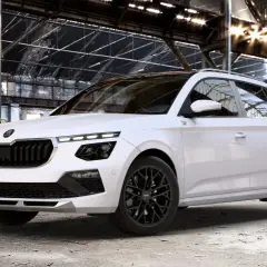Biała Skoda Kamiq Monte Carlo z czarnymi felgami i detalami, zaparkowana w opuszczonej hali przemysłowej z graffiti.