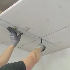 Handwerker bearbeitet Decke mit Rigipsplatten. Die Dicke der Platten ist entscheidend für Stabilität und Dämmung.