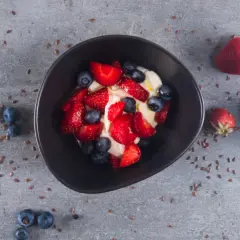 Schüssel mit cremigem low carb Joghurt, garniert mit frischen Erdbeeren und Blaubeeren. Leinsamen verstreut.