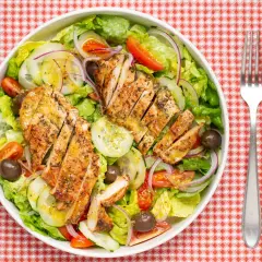 Deliciosa ensalada de pollo a la parrilla con lechuga, tomate, pepino, cebolla morada y aceitunas.