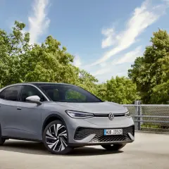 Szary VW ID.5 z czarnym dachem stoi na tle zielonych drzew i błękitnego nieba.