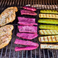 Deux blancs de poulet au barbecue, accompagnés de tranches de patate douce violette et de courgettes grillées, sur une grille.