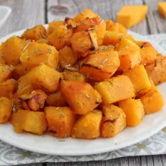Zucca in friggitrice ad aria, dorata e profumata, servita su un piatto bianco con erbe aromatiche.