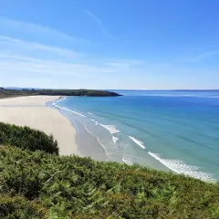 Vue panoramique d'une plage trez bellec, avec sable clair, mer bleue et végétation verdoyante au premier plan.