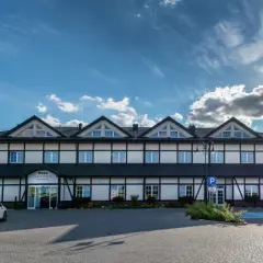 Hotel z białymi ścianami i czarnymi belkami, trzy gwiazdki na fladze, parking.