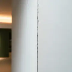 Dettaglio di una crepa su giunti cartongesso, con uno sfondo sfocato di un interno moderno.