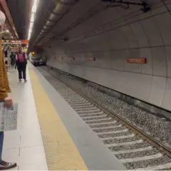 Uomo attende treno alla stazione Valle Aurelia Termini, con giornale in mano.