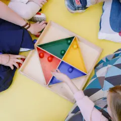 Dzieci i opiekunka bawią się kolorowymi kulkami w drewnianej układance.