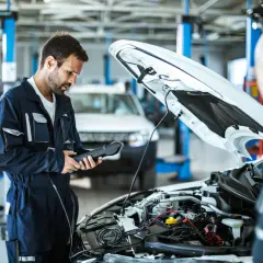 Mecánico revisa el motor de un coche diesel con un escáner. El capó está abierto, mostrando el complejo sistema.