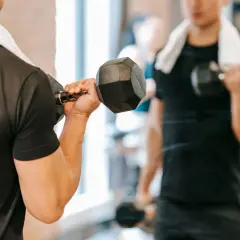 Mężczyzna ćwiczy biceps z hantlem, zaczynając dzień od treningu na czczo. W tle widać jego odbicie w lustrze.