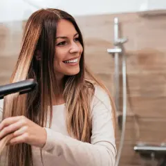 Mujer sonriendo mientras se alisa el pelo con una plancha, buscando el secreto de como alisar el pelo para siempre.