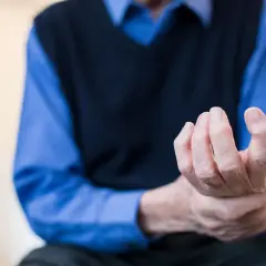 Dłoń starszego mężczyzny z widocznym drżeniem rąk. Palce lekko zgięte, ukazujące trudności w utrzymaniu stabilności.